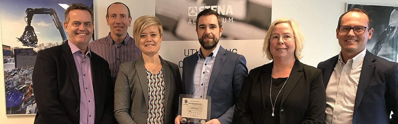 Sex personer står tillsammans, ler och håller en prisplakett i sina händer