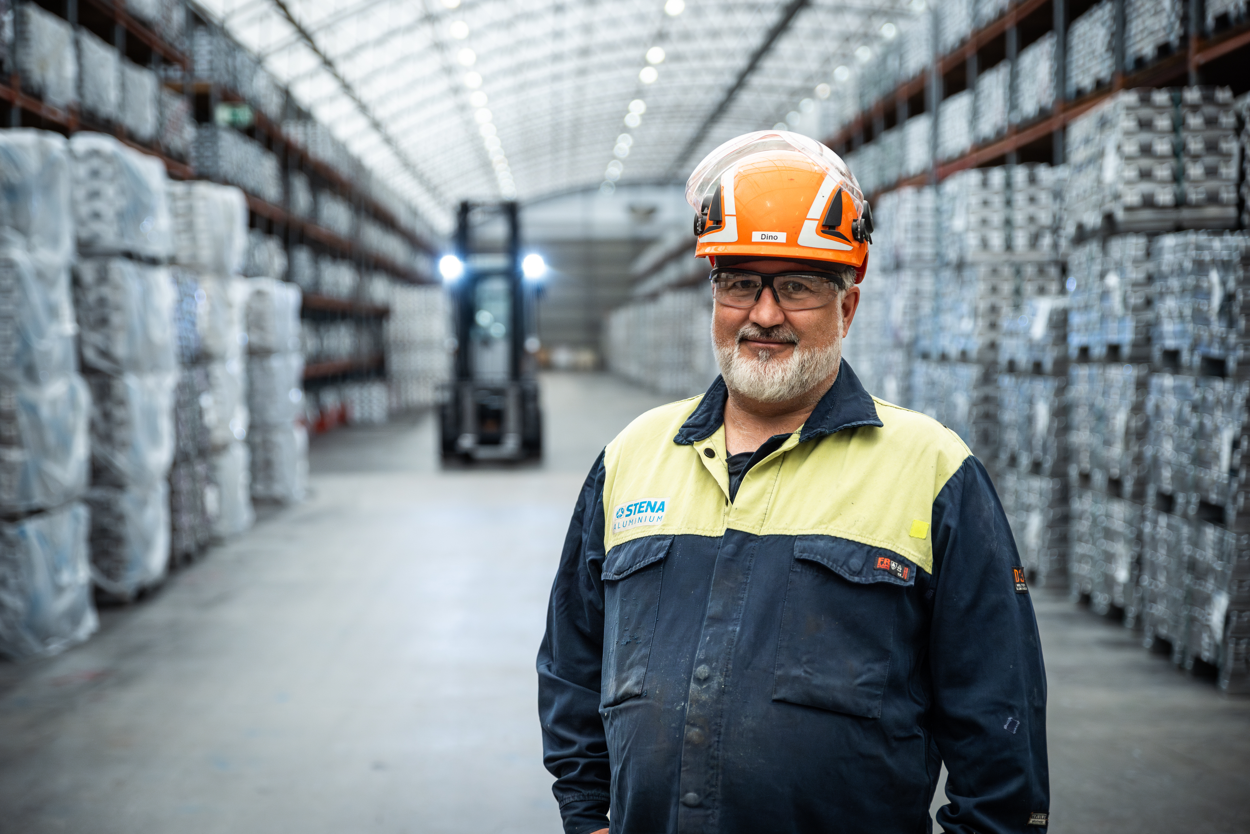 Stena Aluminium anställd som ler mot kameran, stående i lagerlokalen i Älmhult, Sverige.