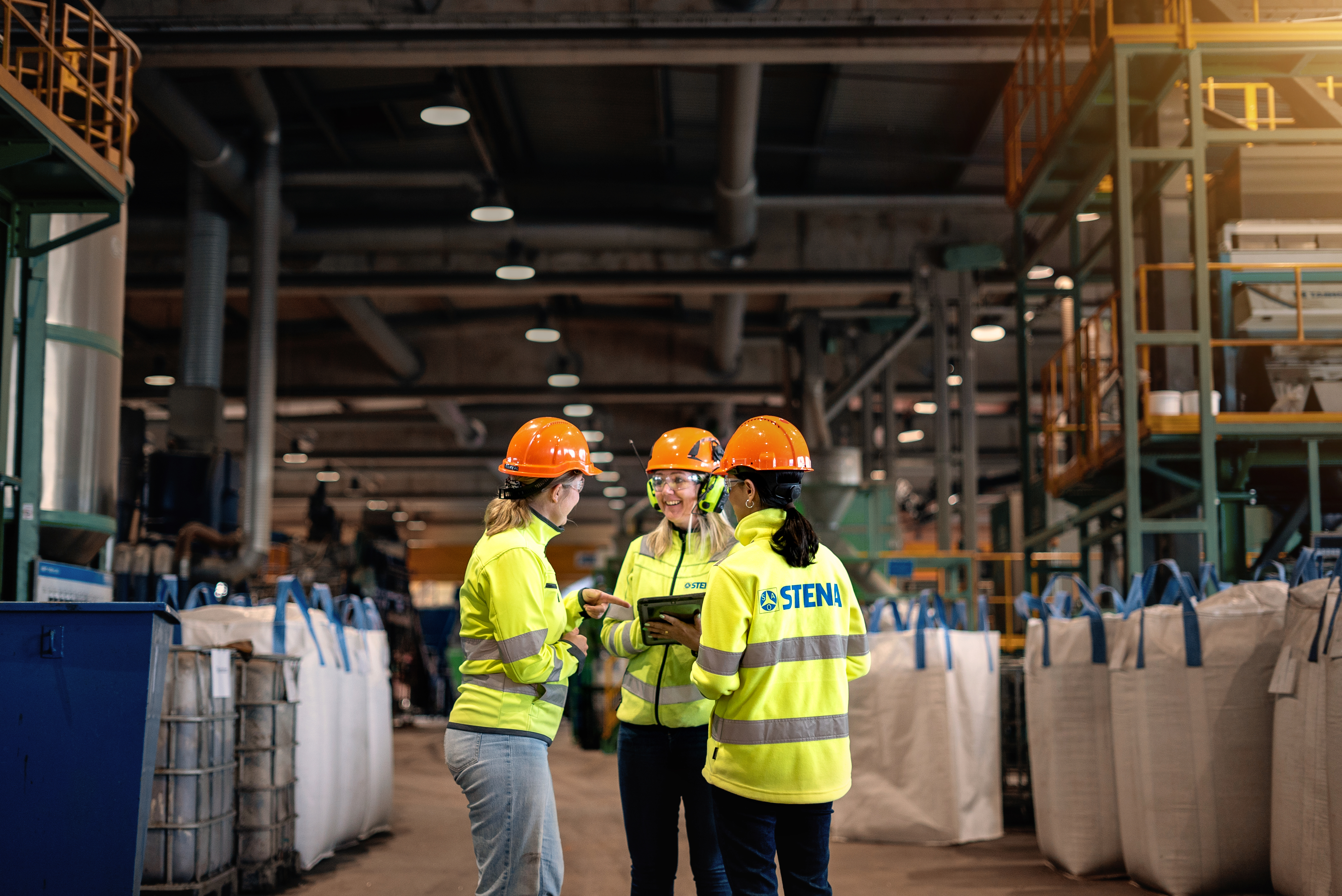 A group of three Stena Metall Group employees talk at Stena Nordic Recycling Center, Halmstad, Sweden.